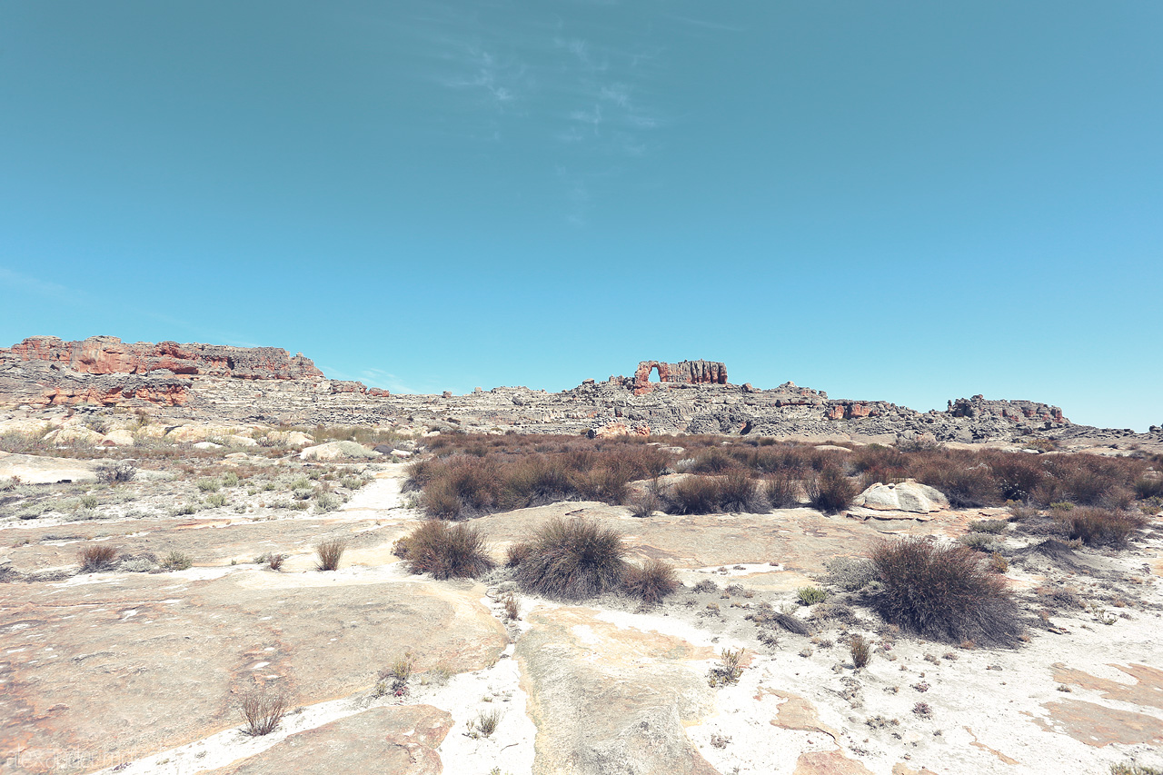 Kaleidoscope of Rugged Earth Foto von Sunlit rock formations and hardy shrubs under a vast sky in Cederberg, South Africa. A stark yet stunning natural tapestry.